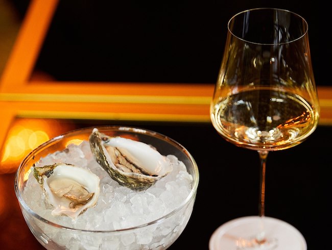 Una copa de vino blanco servida al lado de dos ostras